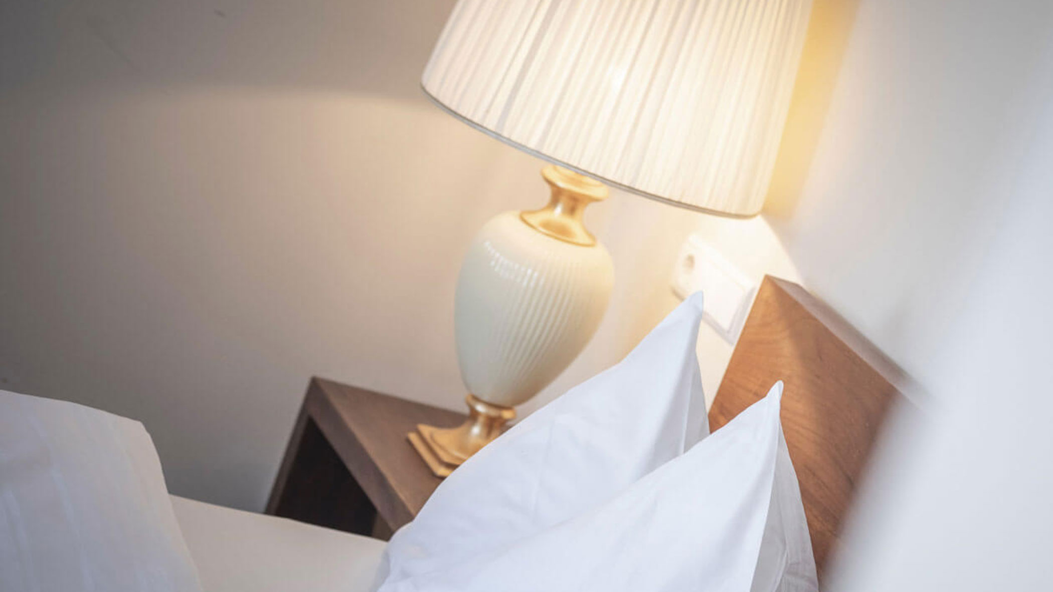Ein Nachttisch mit einer weißen Lampe und ein Teil eines Bettes mit weißen Kissen und Laken. - Hotel Fameli
