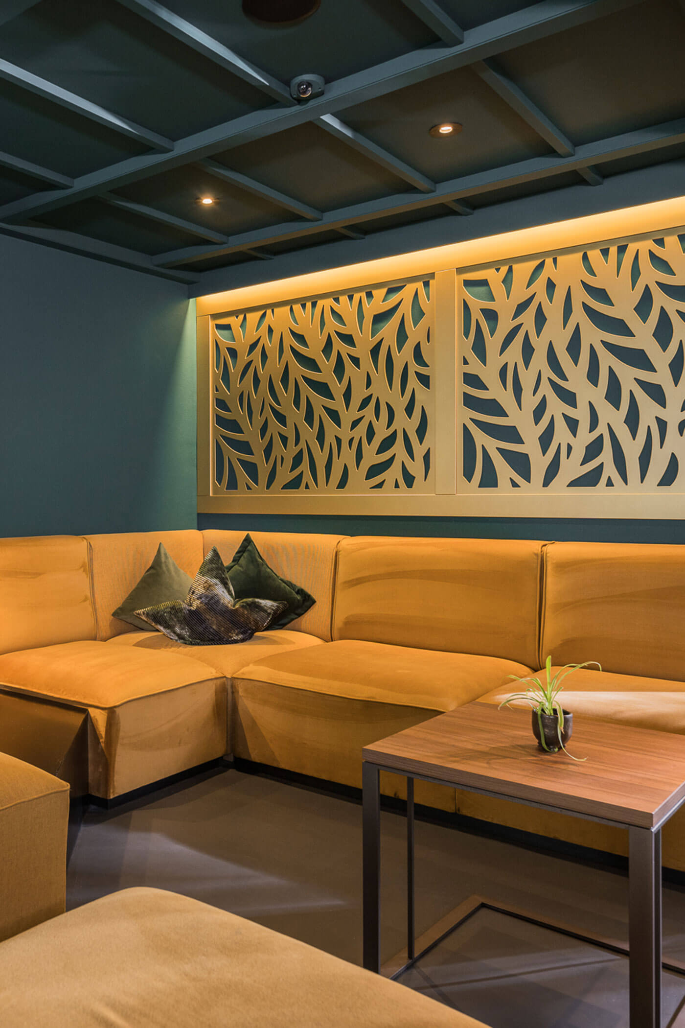 Modernes Wohnzimmer mit senfgelbem Sektionssofa, dekorativem Blattpaneel und kleinem Tisch mit einer Pflanze. - Hotel Fameli