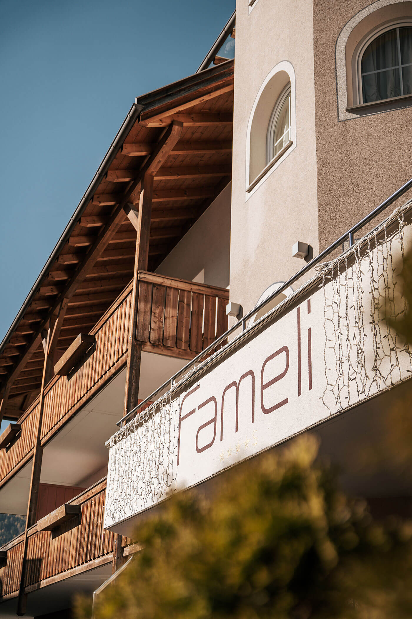 Hotel mit Holzbalkonen und einem Schild mit der Aufschrift Fameli an einem sonnigen Tag. - Hotel Fameli