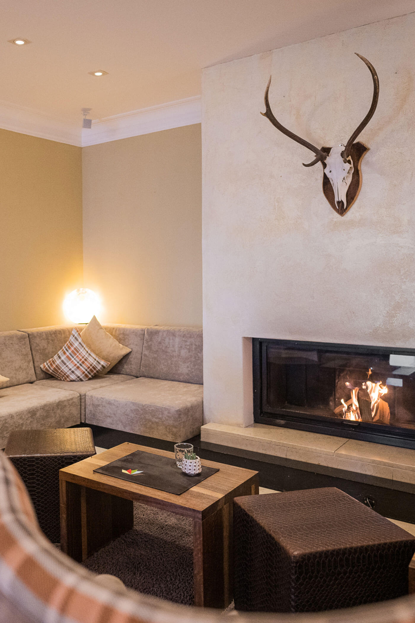 Gemütliches Wohnzimmer mit Kamin, Geweihdekor, Sektionssofa und Holztischen mit Sitzwürfeln. - Hotel Fameli