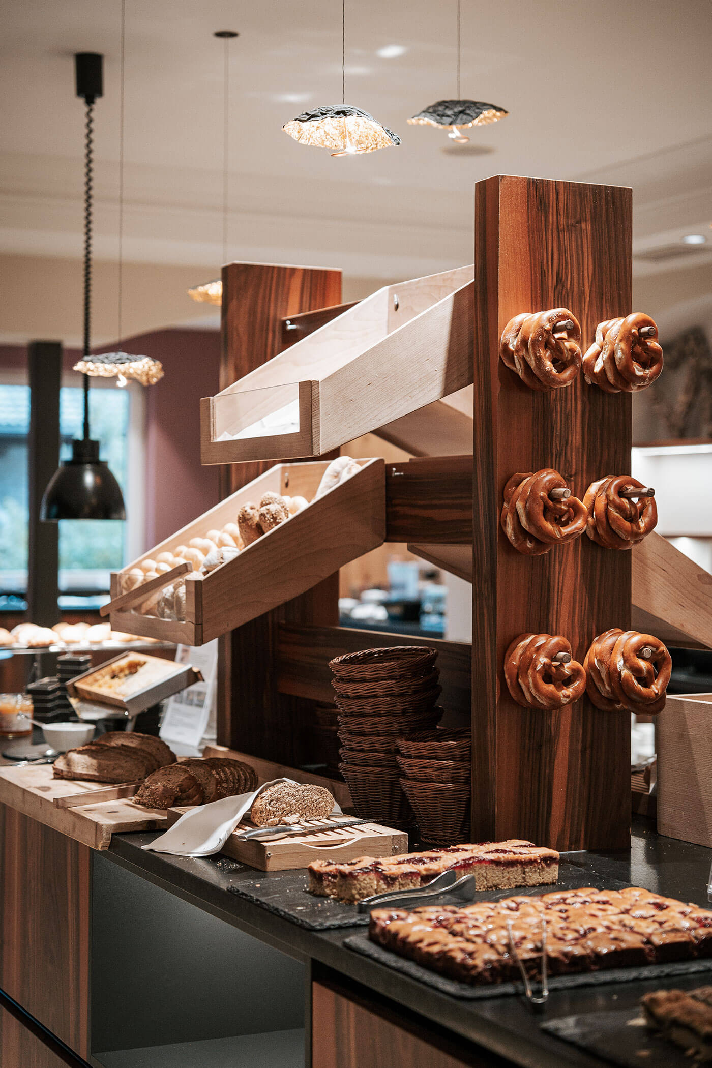 Eine Bäckereiauslage mit Brezeln an Haken, Brot, Gebäck und Backwaren auf Holzregalen und Tabletts. - Hotel Fameli