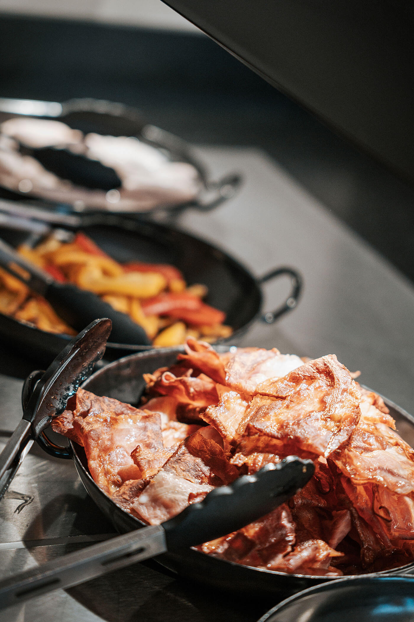 Knuspriger Speck, gebratene Kartoffelspalten und in Scheiben geschnittener Truthahn in Serviertabletts mit Zangen am Buffet. - Hotel Fameli