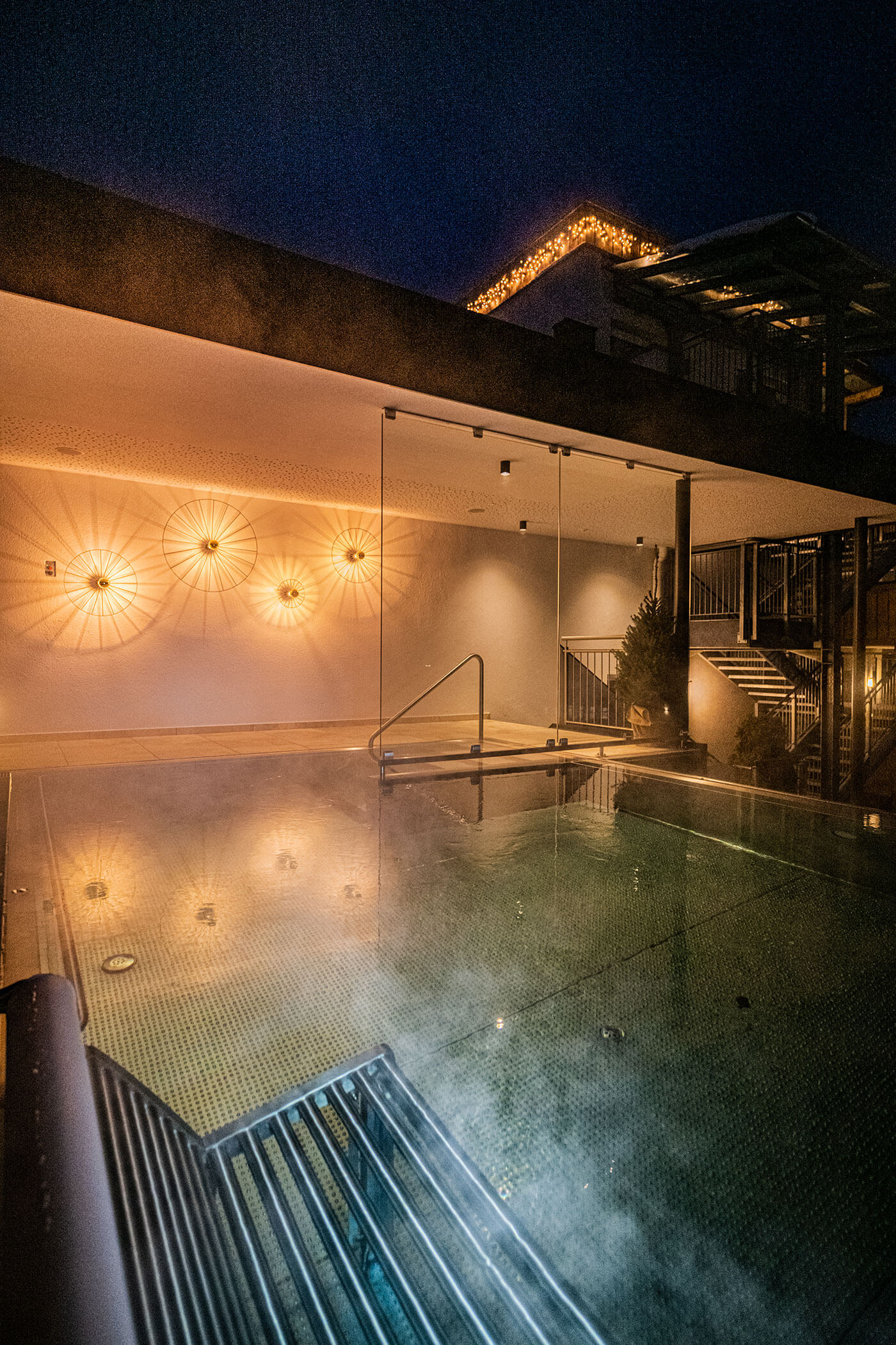 Ein beleuchteter Außenpool bei Nacht, mit modernen Wandleuchten und warmer Umgebungsbeleuchtung am Gebäude. - Hotel Fameli