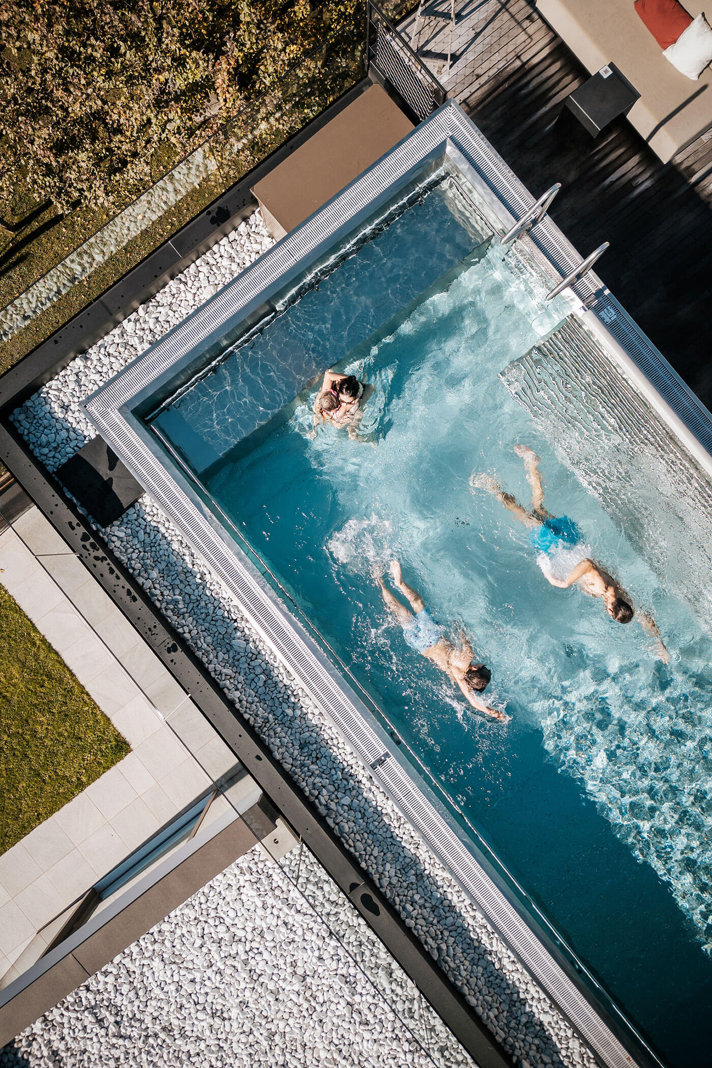 Luftaufnahme von drei Personen, die in einem rechteckigen Außenpool neben einer Liegewiese schwimmen. - Hotel Fameli