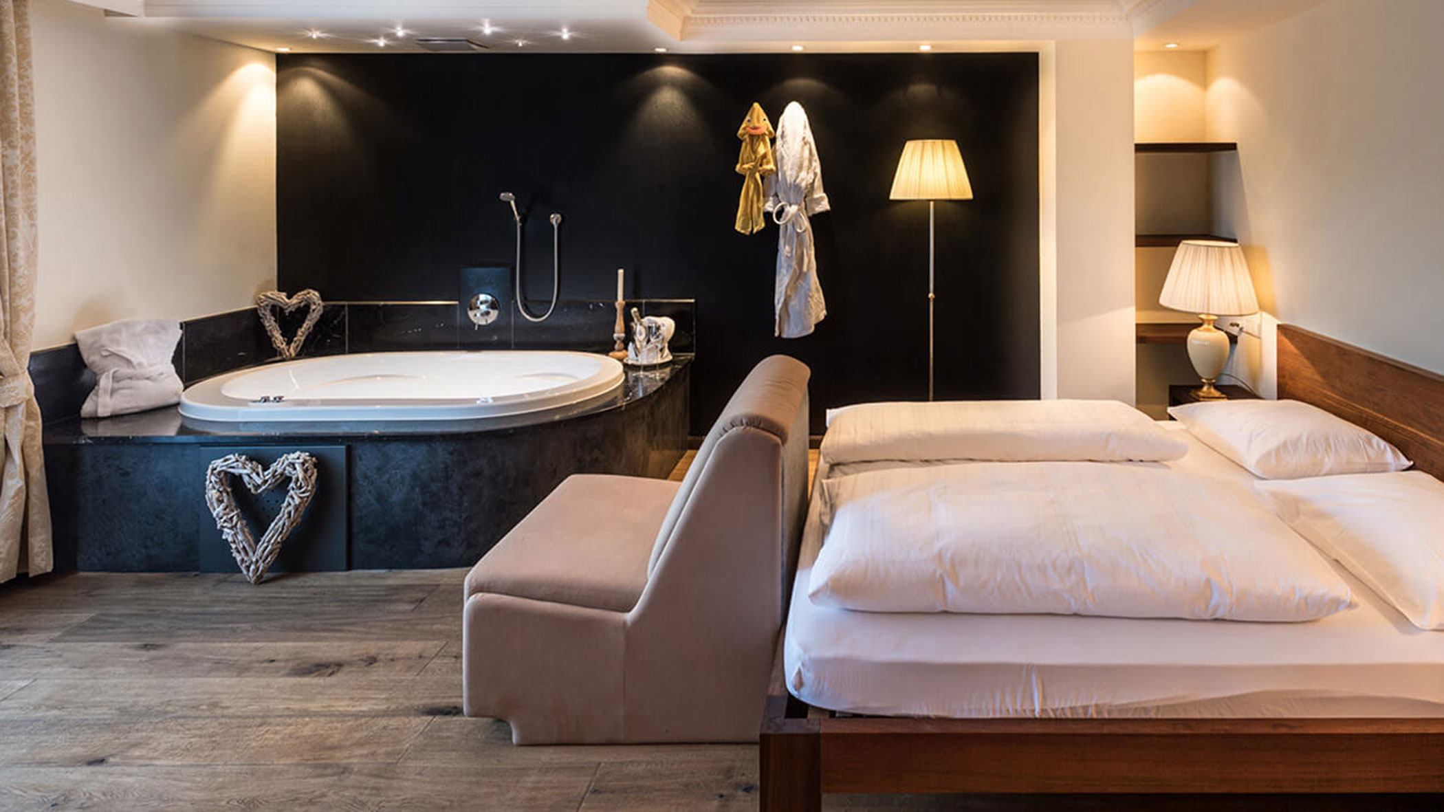 Modernes Hotelzimmer mit großem Bett, Sofa, Badewanne im Zimmer, Bademänteln und warmer Beleuchtung. - Hotel Fameli