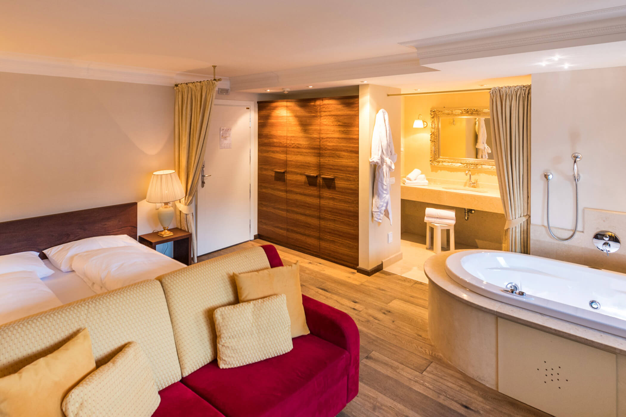 Hotelzimmer mit Doppelbett, rotem Sofa, großem Holzschrank und Badezimmer mit Jacuzzi-Wanne. - Hotel Fameli