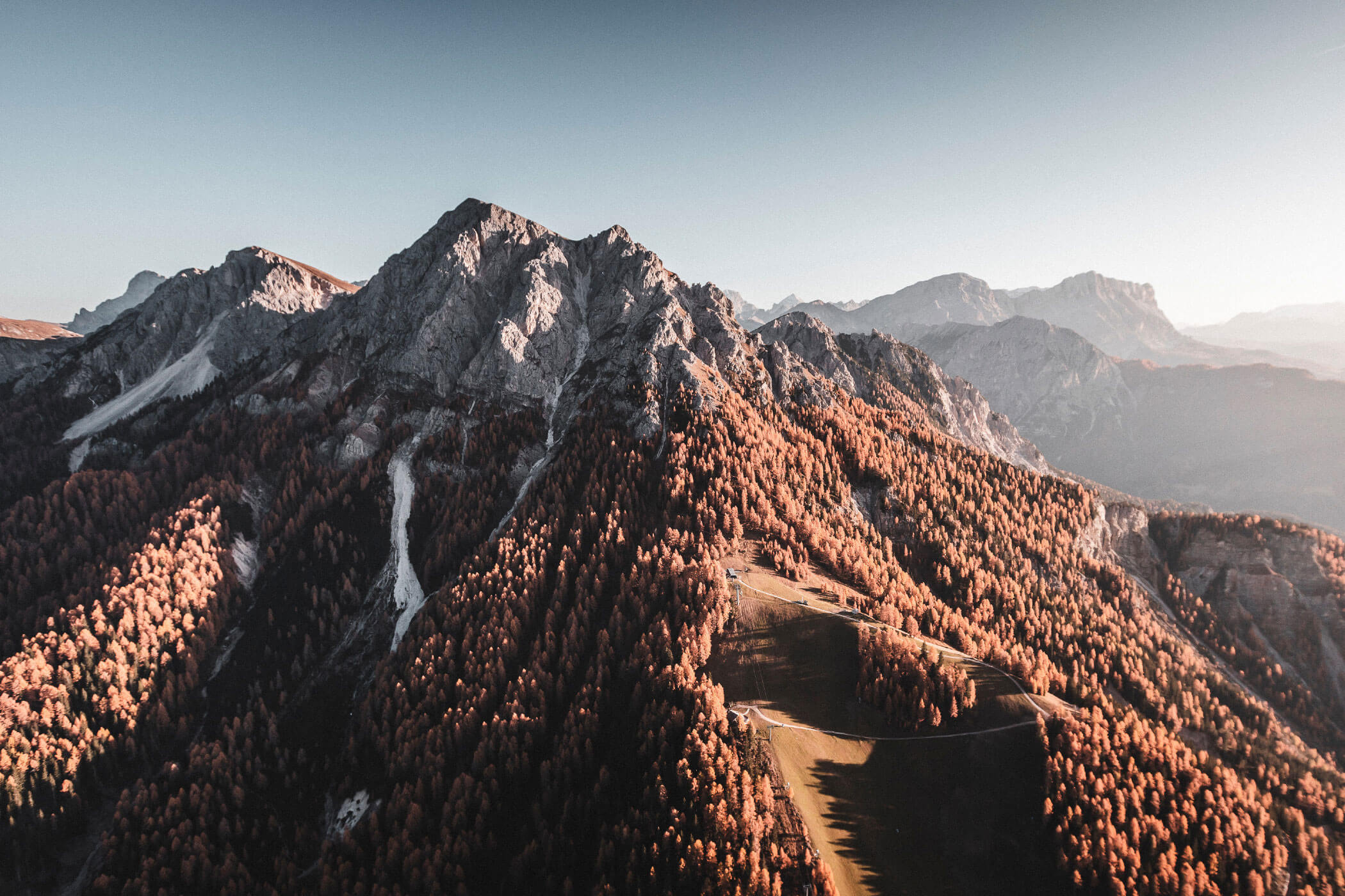 Luftaufnahme von zerklüfteten Bergen mit herbstlich gefärbten Bäumen unter einem klaren Himmel. - Hotel Fameli