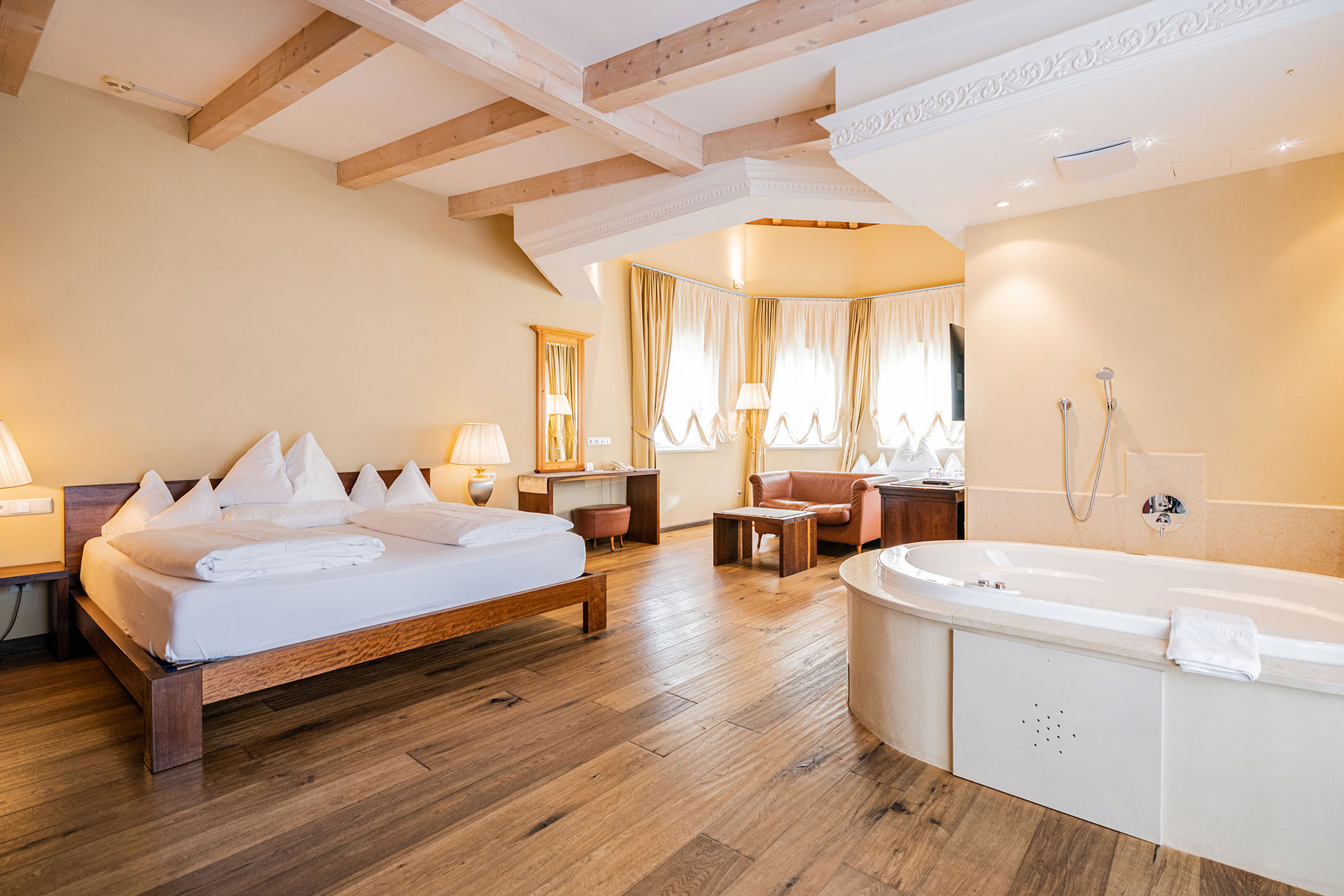 Geräumiges Hotelzimmer mit Doppelbett, großer runder Badewanne, Holzboden und Sitzecke am Fenster. - Hotel Fameli