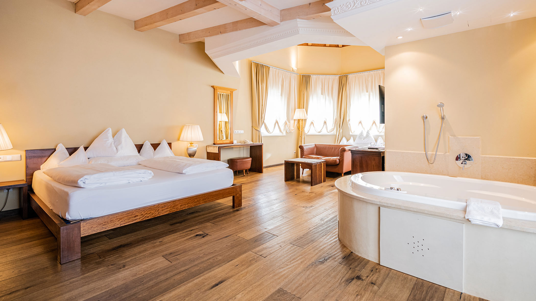 Geräumiges Hotelzimmer mit Doppelbett, Holzboden, gemütlicher Sitzecke und einer großen Badewanne. - Hotel Fameli