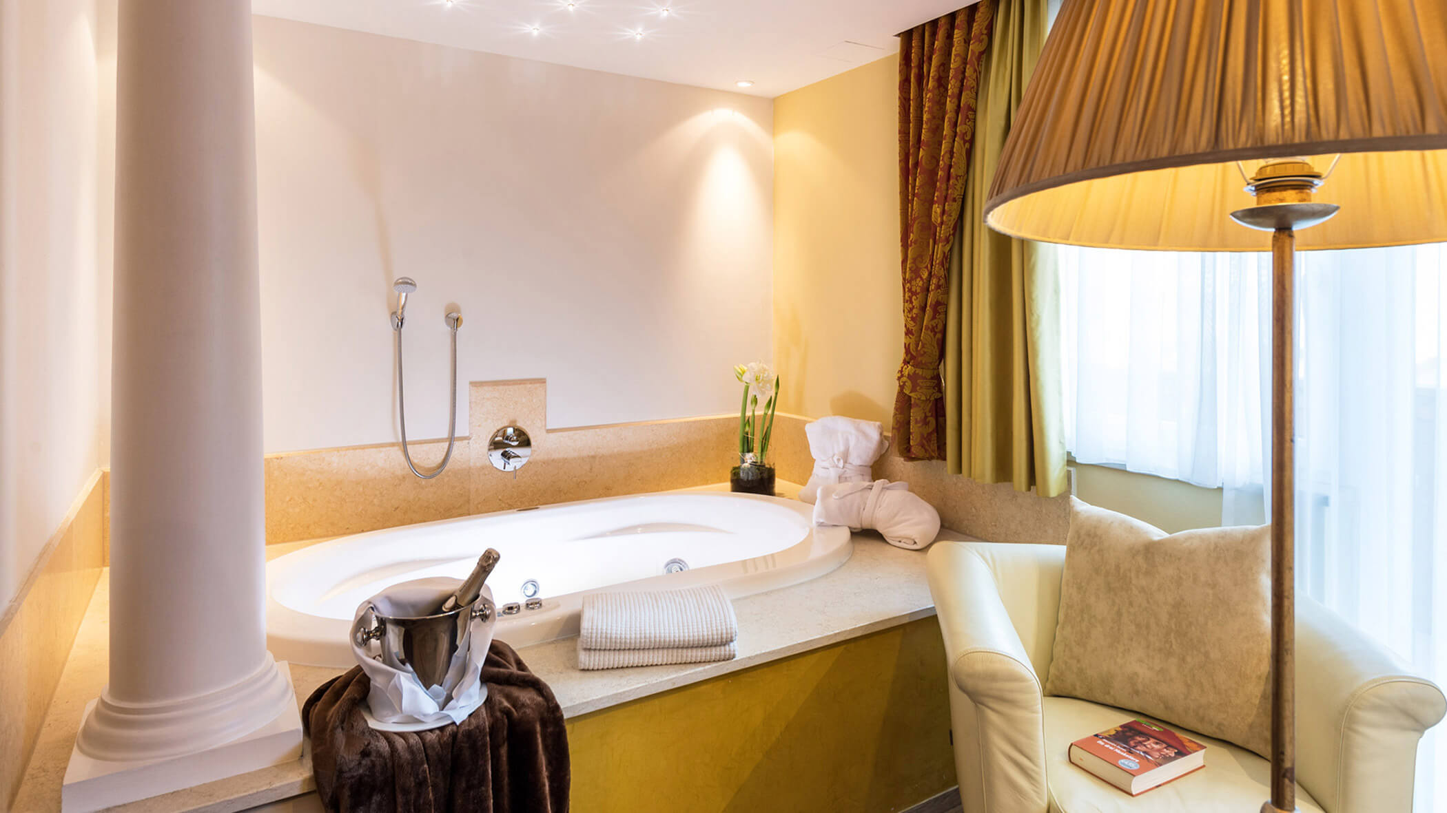 Luxuriöses Badezimmer mit großer Badewanne, Handtuch, Wein in einem Eiskübel, Sessel und Stehlampe. - Hotel Fameli