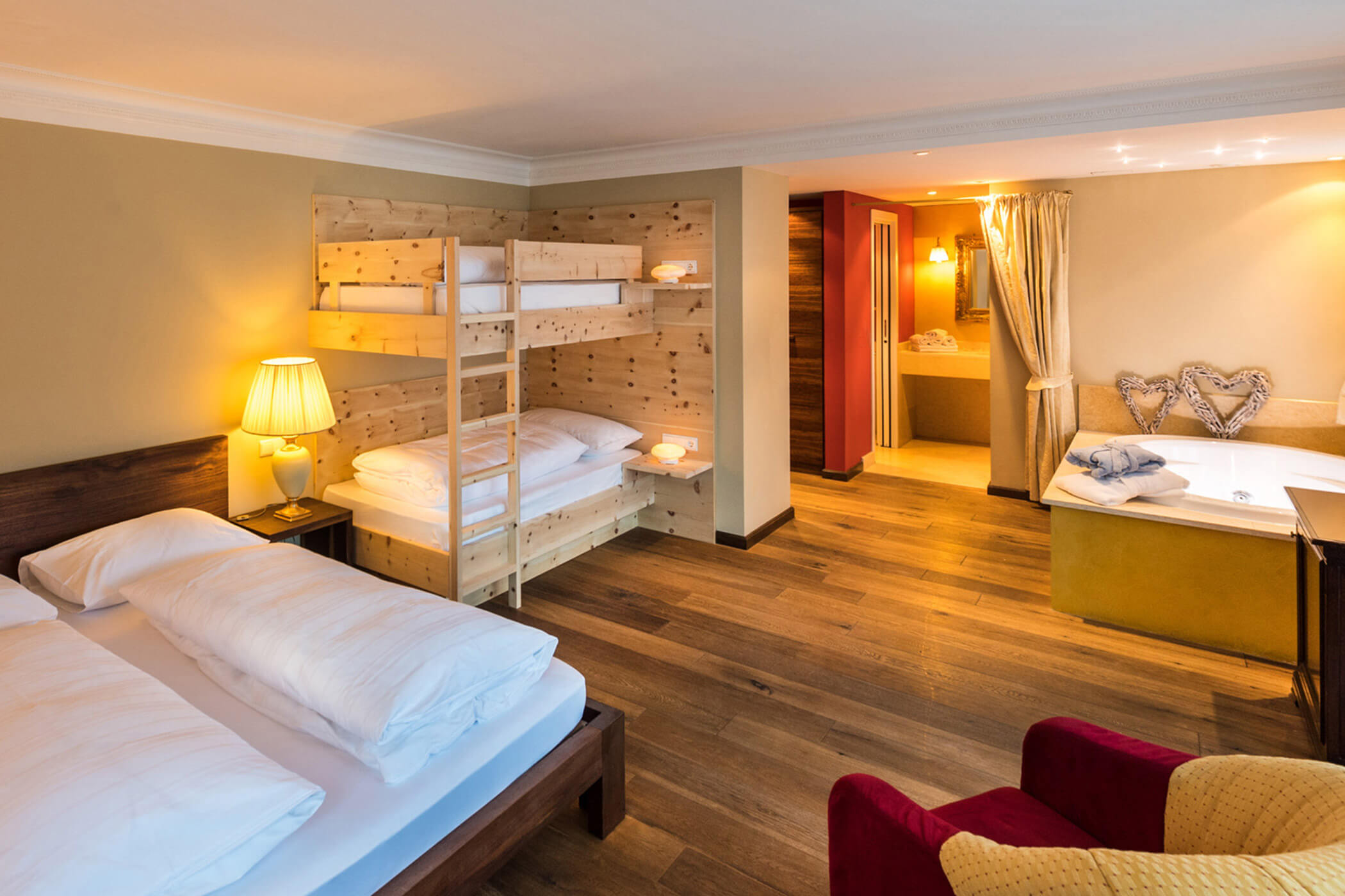 Hotelzimmer mit Doppelbett, Etagenbett, Sessel, Lampe und offenem Bad mit Whirlpool. - Hotel Fameli